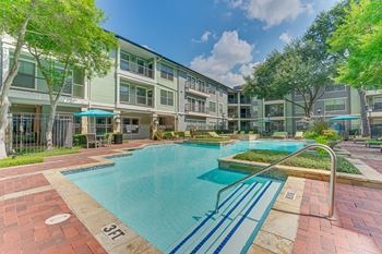 A swimming pool surrounded by a brick walkway and trees. at Easton Apartments, Dallas, Texas